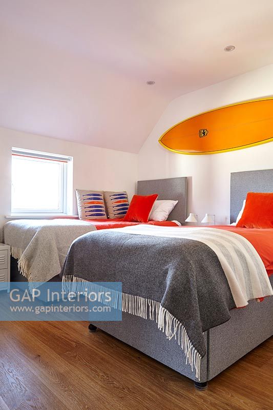 Bright orange surfboard above twin beds in modern bedroom 