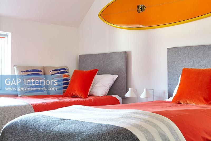 Bright orange surfboard above twin beds in modern bedroom 