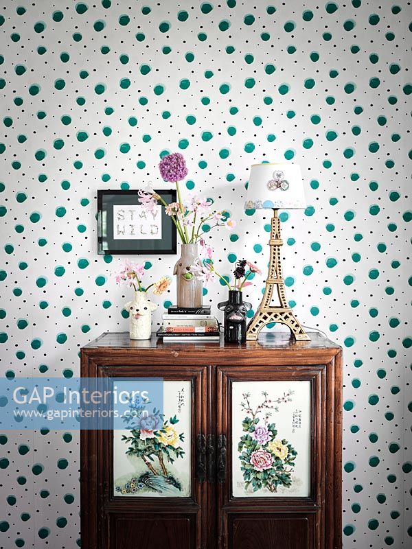 Vintage cabinet with floral paneled doors next to spotty wallpaper 