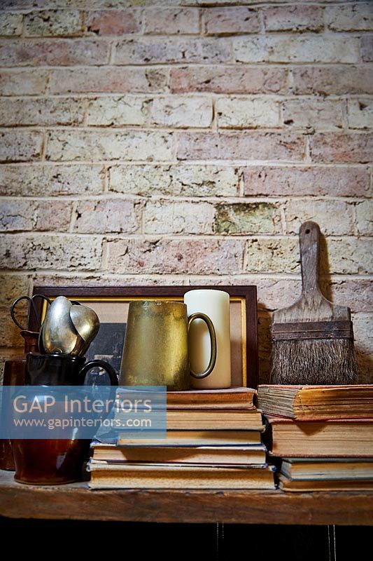 Books and ornaments on wooden shelf against exposed brick wall 
