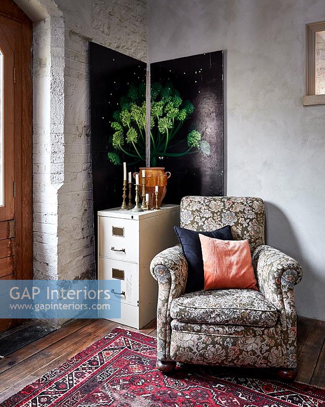 Floral armchair in corner of country living room with decorative wall panels 