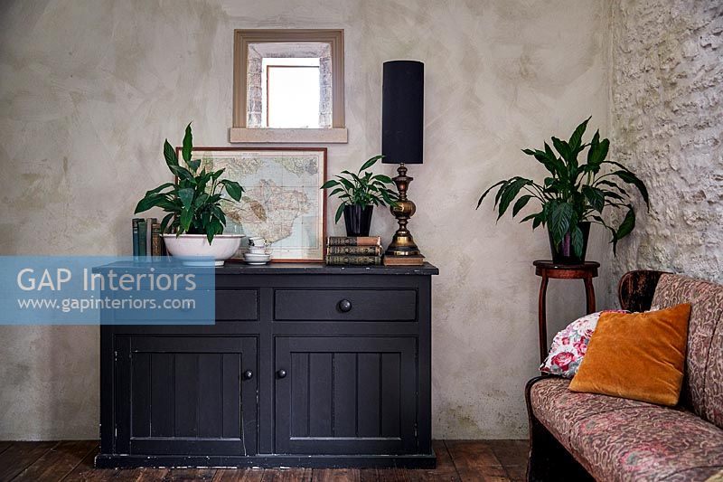 Black wooden sideboard in country living room with bare plaster wall