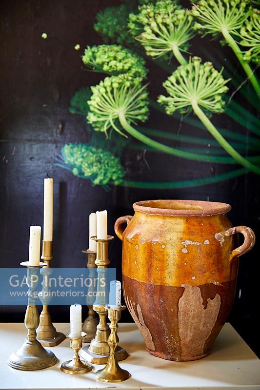 Collection of brass candlesticks and a ceramic pot next to painting 