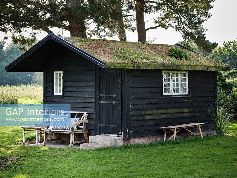 Wooden summer house with living roof and rustic bench outside 