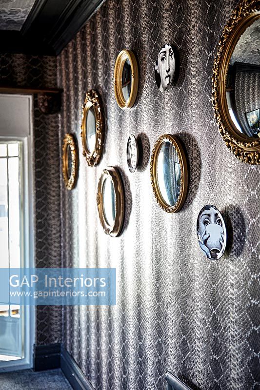 Display of mirrors and plats on wallpapered wall 