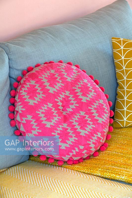 Bright pink cushion on blue and yellow sofa 