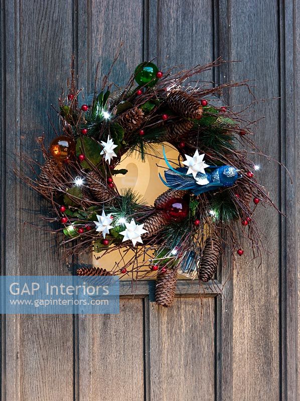 Wreath on wooden front door with modern decorations and fairy lights 