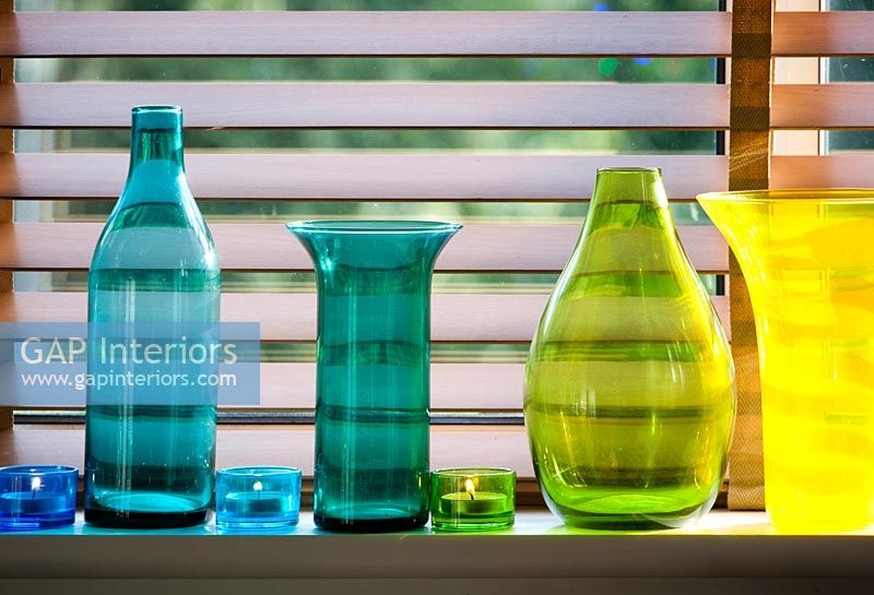 Collection of colourful glassware on windowsill with tealight candles 