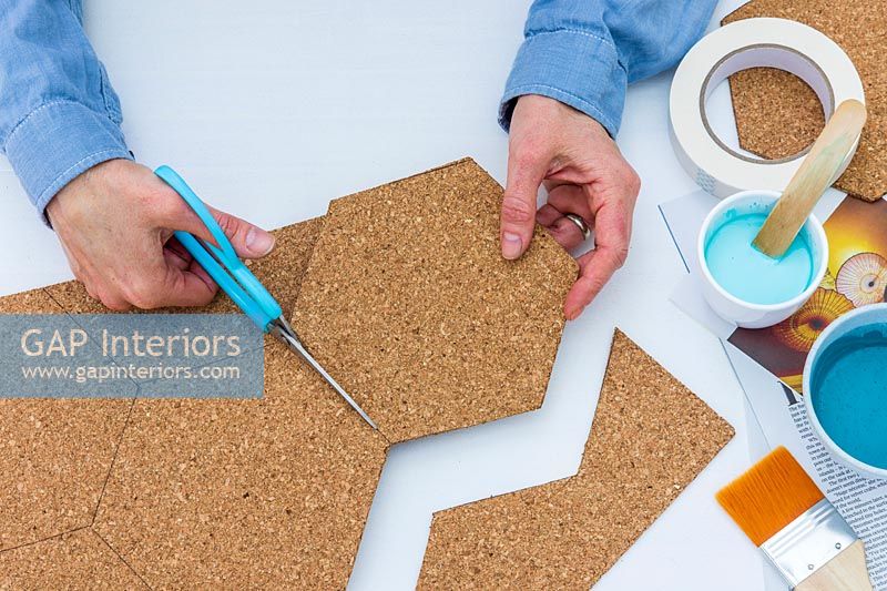 Woman using scissors to cut out hexoganal shapes from sheet of cork