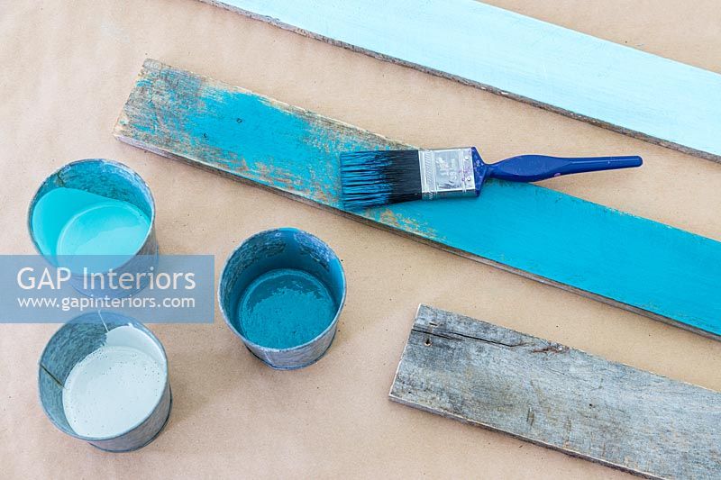 Rustic wooden boards painted in various tones of turqoise including paintbrush and paint pots
