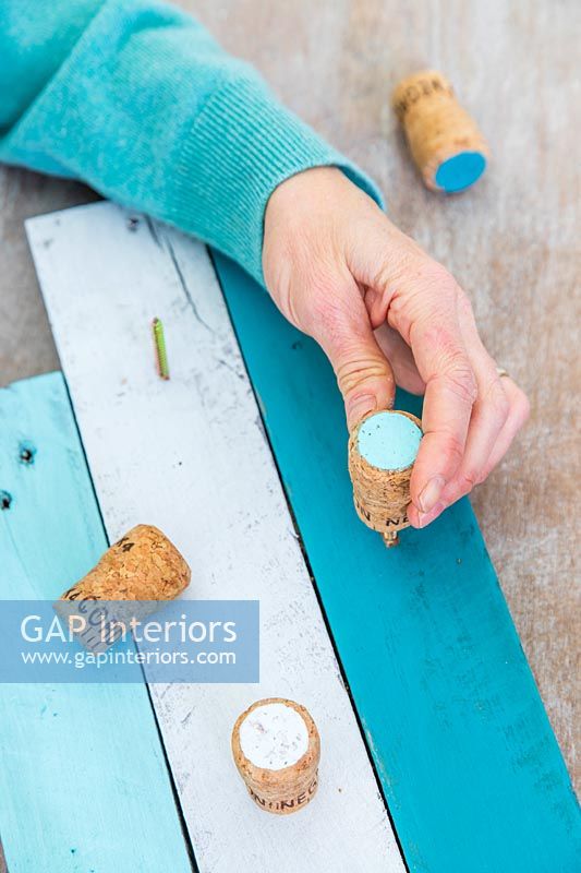 Woman screwing painted cork tops onto prepared timber strips to make a jewellery display unit