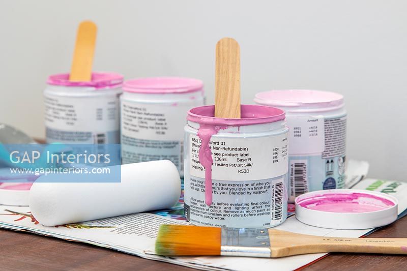 Paint pots with various shades of dusty pink, paint brushes and rollers