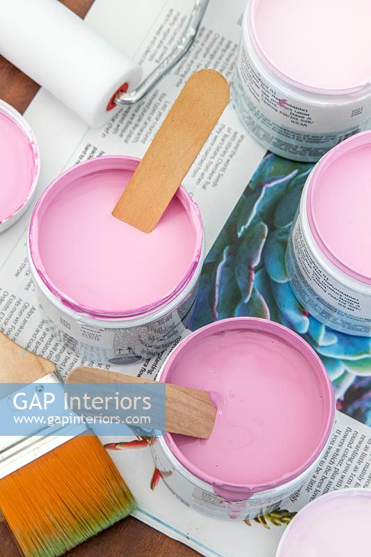 Paint pots with various shades of dusty pink, paint brushes and rollers