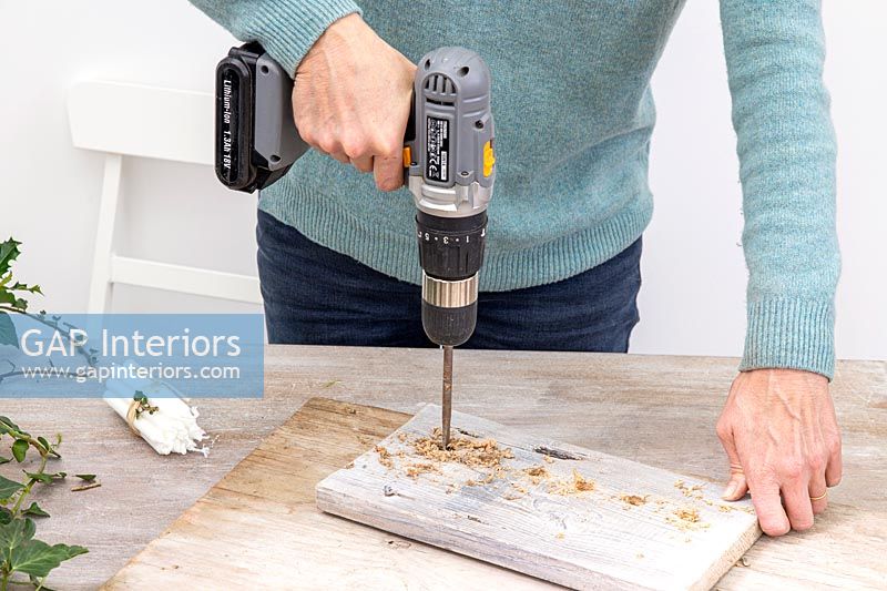 Woman using electric drill with large drill bit to make candle holes in wood