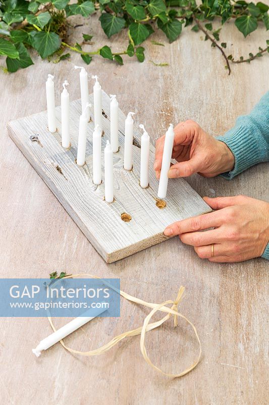 woman placing candles into drilled holes in wood