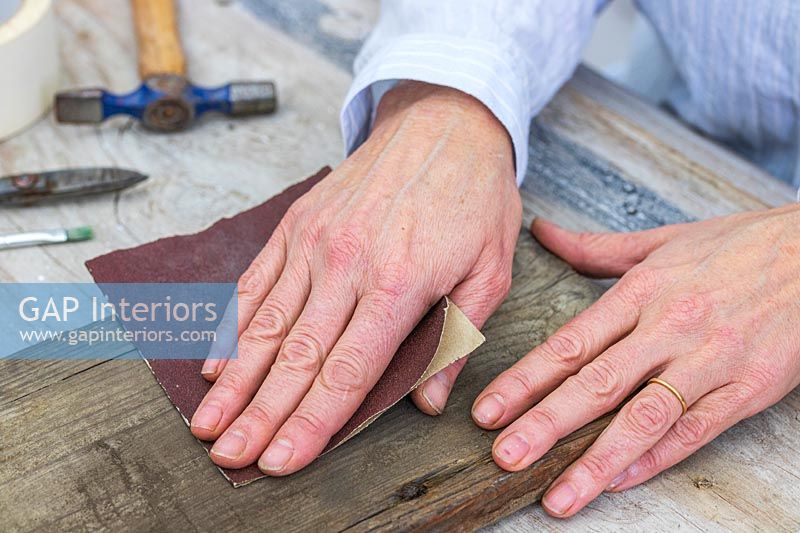 Woman sanding down piece of wood with fine sandpaper