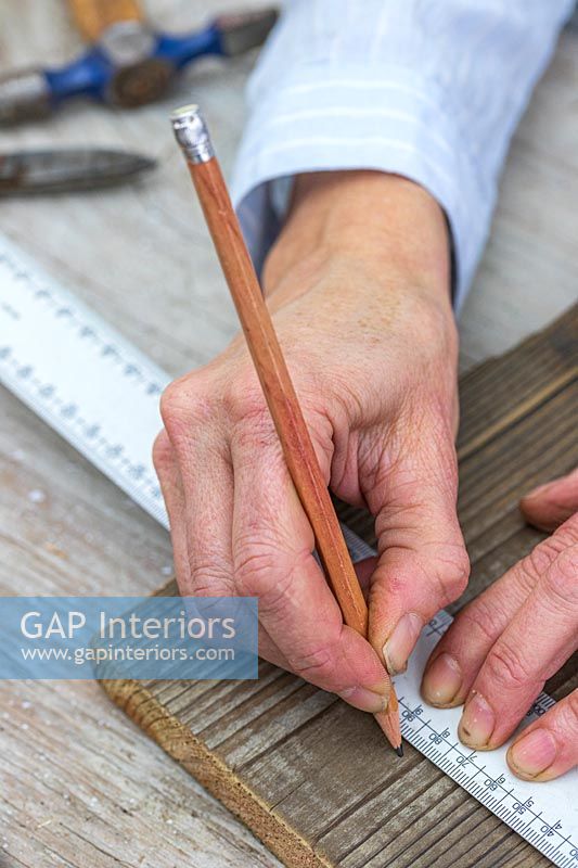 Close up detail of woman using pencil and ruler to mark piece of wood