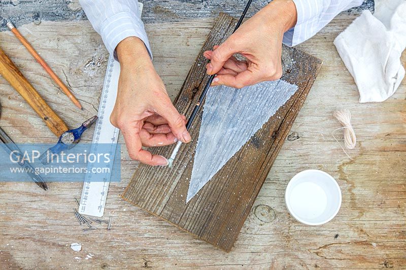 Woman using a paint brush to flick paint onto wood to simulate snow falling