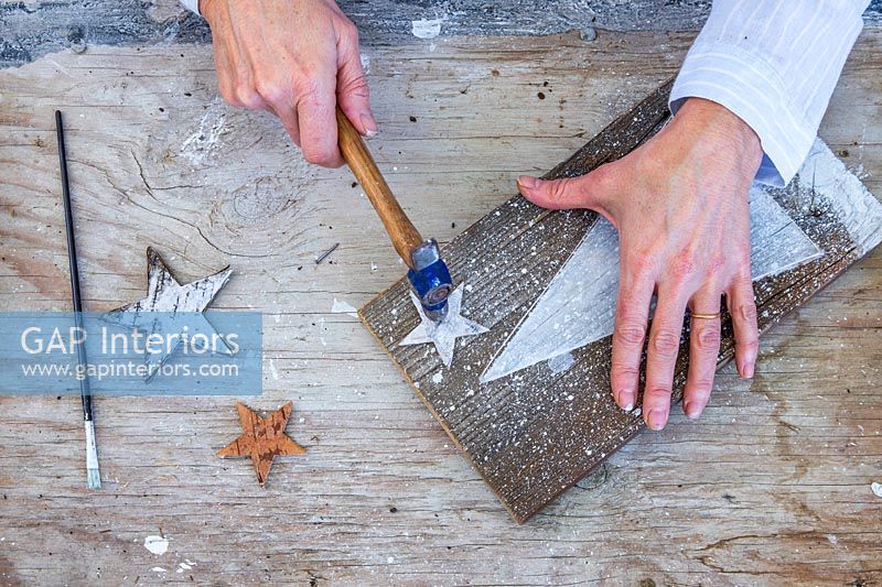 Woman fixing painted wooden stars onto board using a hammer and small tack