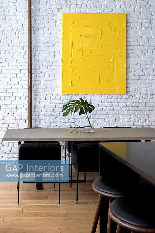 Modern dining room with white painted brickwork wall and yellow artwork