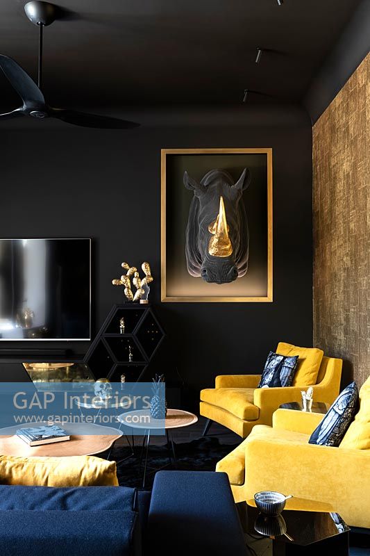 Dark painted walls in modern living room with gold feature wall and fabric Rhino trophy head 