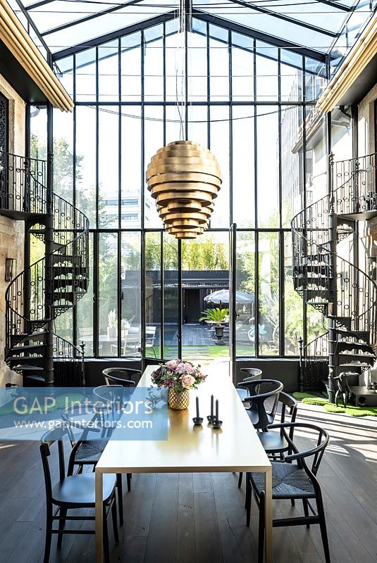 Contemporary dining room in glazed building with metal spiral staircases on both sides and view to garden