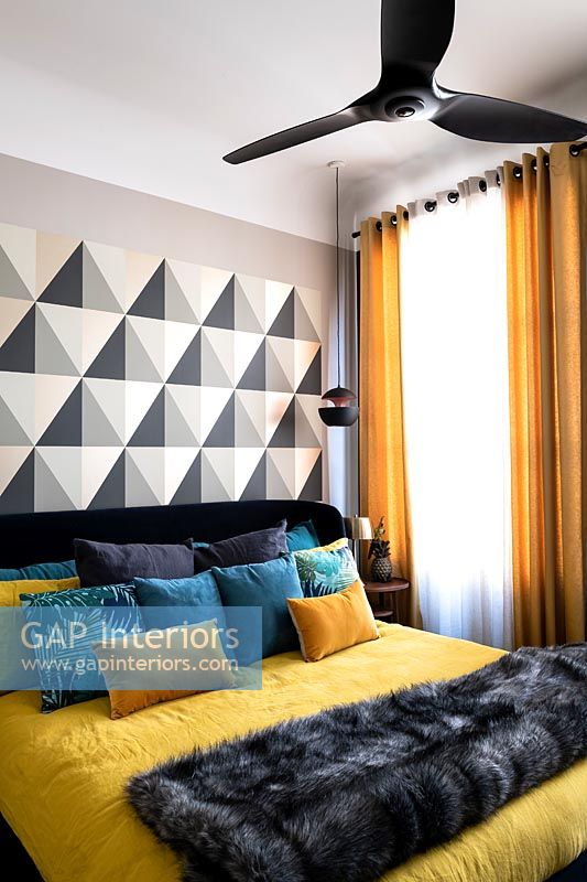 Modern bedroom with patterned feature wall colourful bedding and black ceiling fan 