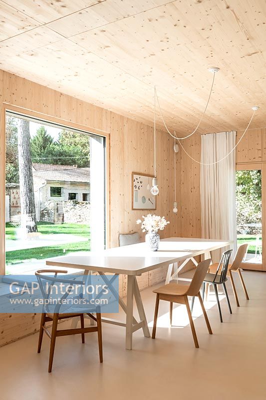 Modern dining room in timber clad house with large picture window with view to garden 
