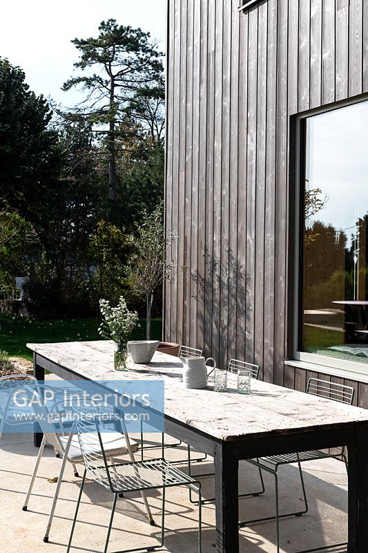 Outdoor dining table on terrace next to modern timber clad house 