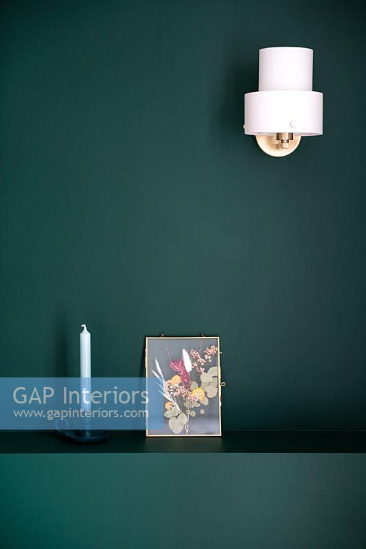 White sconce light on green painted wall with picture and candle 