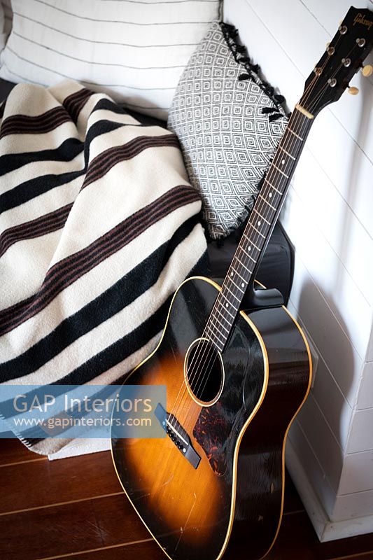 Close up of guitar next to blankets and cushions 
