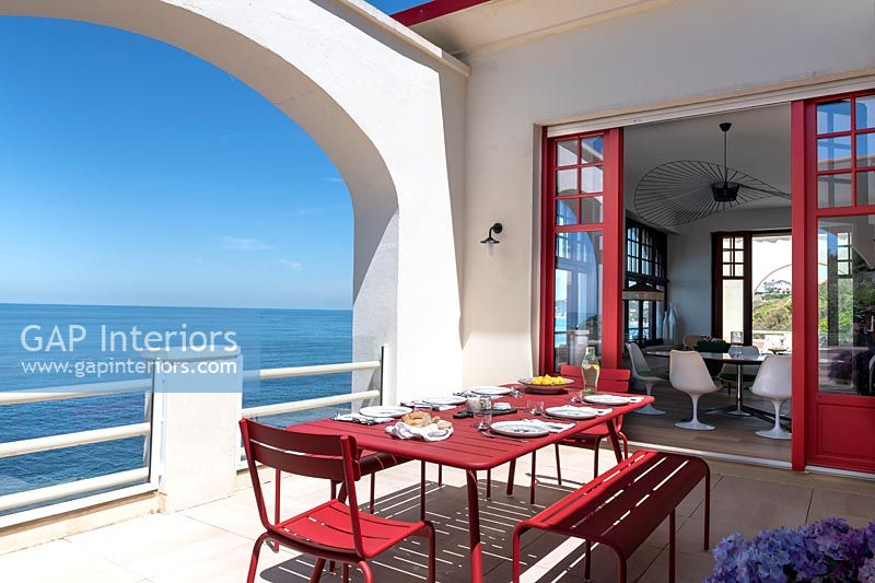 Red dining table on white terrace with sea views 