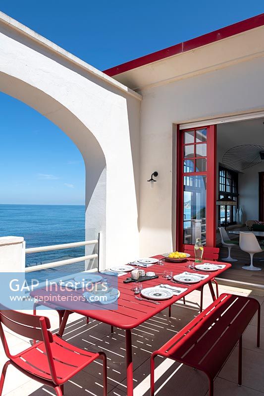 Outdoor dining table laid for lunch on red and white terrace with sea views 