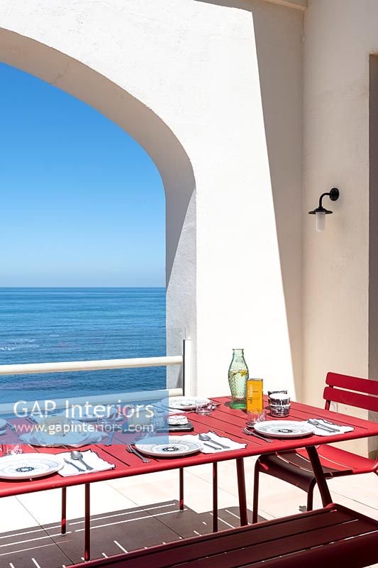Red dining table on white terrace with sea views 