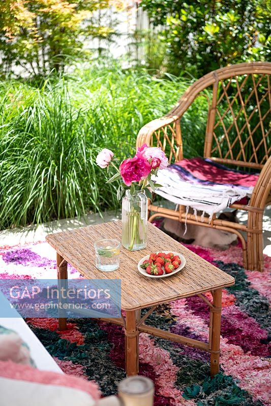 Cane furniture and colourful rug in outdoor living area 