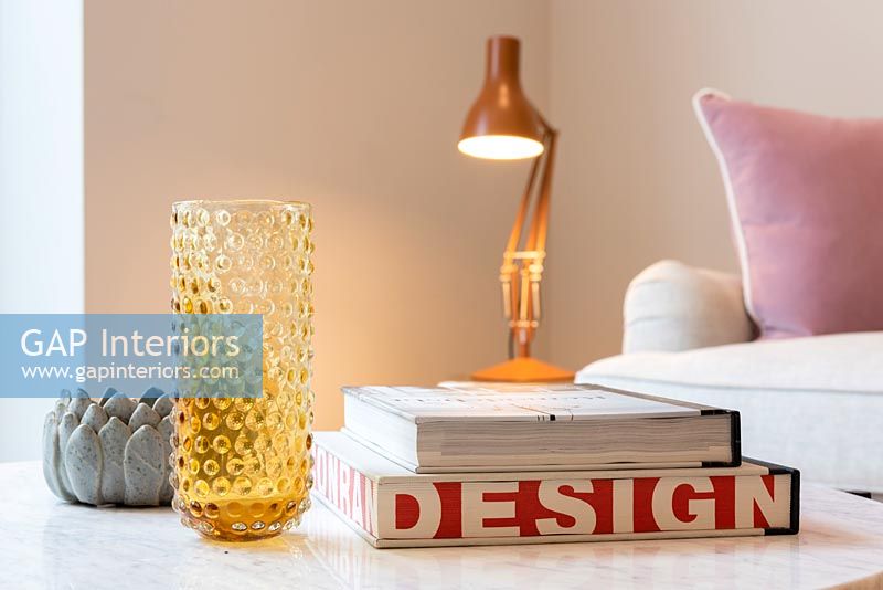 Detail of glassware and books on living room table with lamp in background 