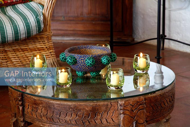 Candles in small glasses on carved wooden coffee table 