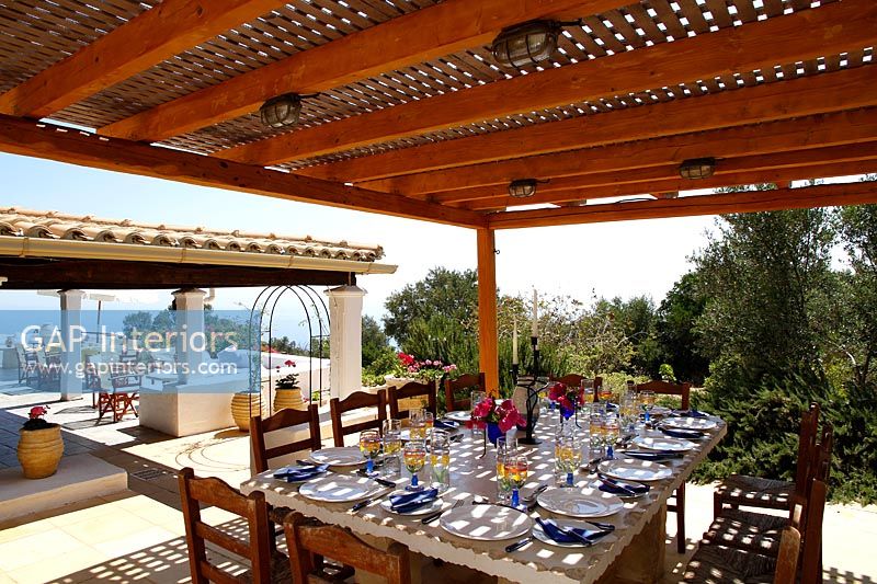 Large dining table under covered terrace laid for lunch in summer 