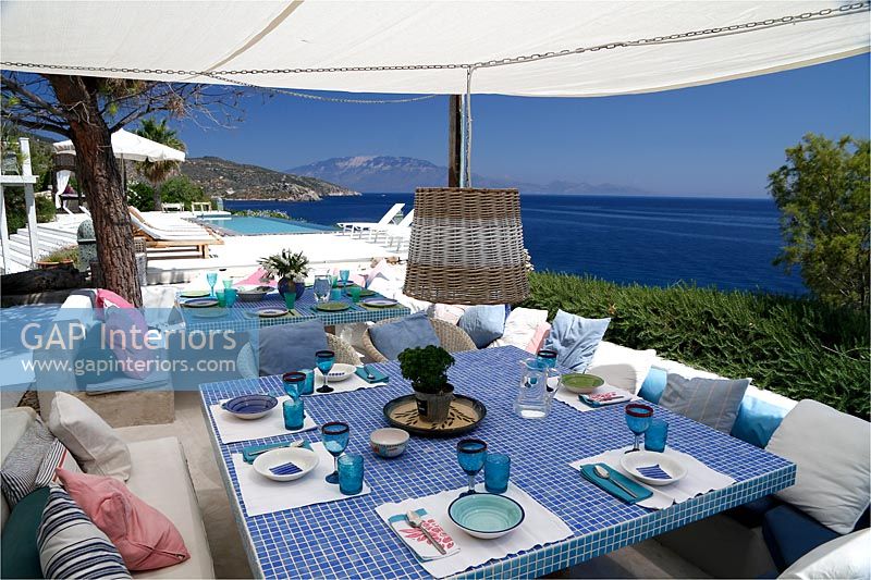 Large tiled outdoor dining table under canopy with coastal views 