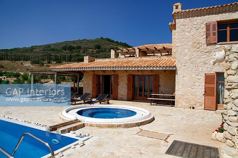 Swimming pool and recliners outside stone cottage with sunken jacuzzi on terrace 