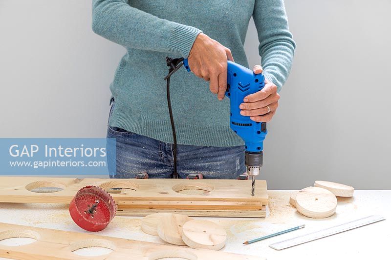 Woman using a drill to make small holes in the corners of the boards to enable hanging