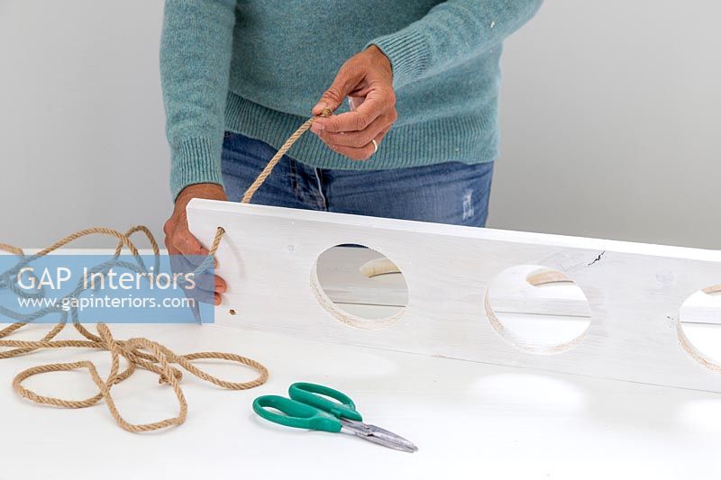 Woman threading cord or rope through the holes made in the corners of the boards