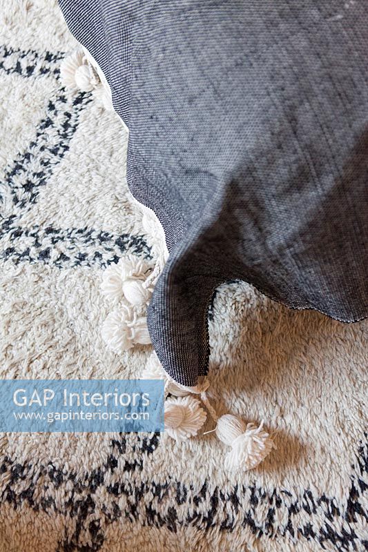 Detail of grey cushion with tassels on black and white rug 