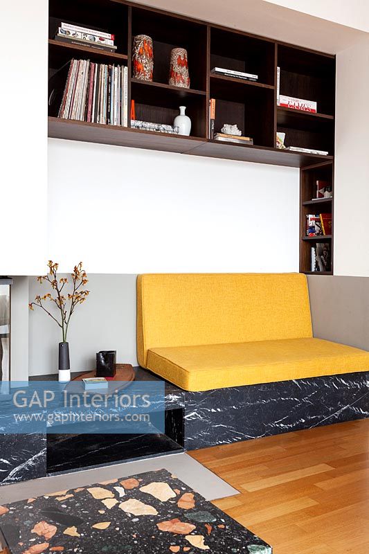 Yellow sofa cushions on built-in seat within alcove with surrounding shelving 