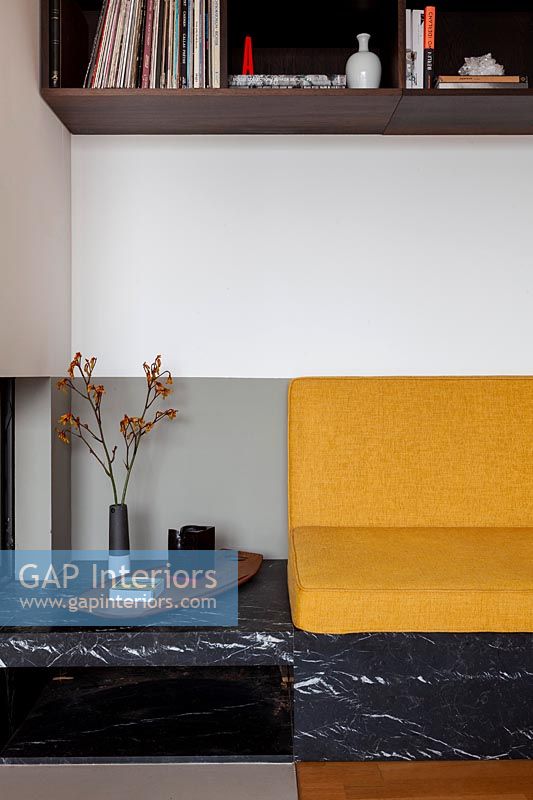 Yellow sofa cushions on built-in seat within alcove with surrounding shelving 