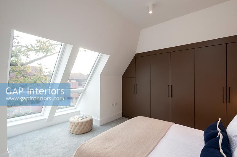 Modern bedroom with pitched roof windows and brown built-in wardrobe 