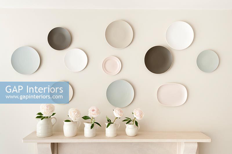 Display of wall mounted plates in muted tones with vases of flowers 