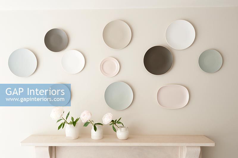 Display of wall mounted plates in muted tones with vases of flowers 