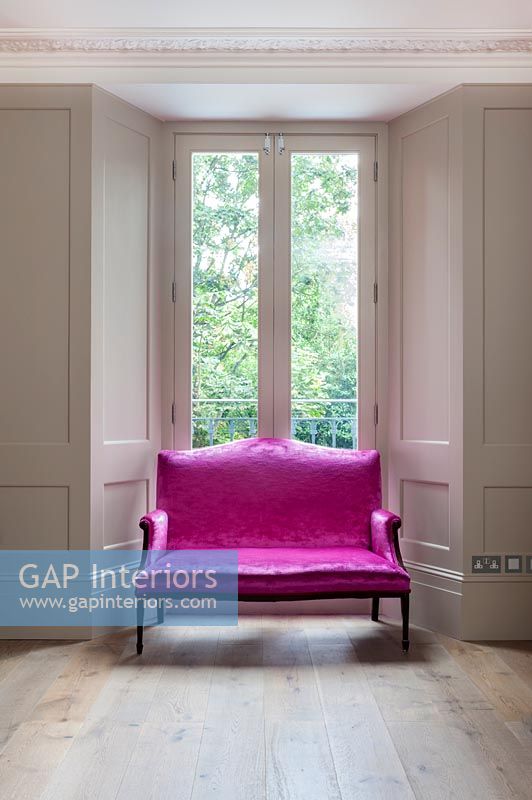 Bright pink sofa next to window in panelled living room 