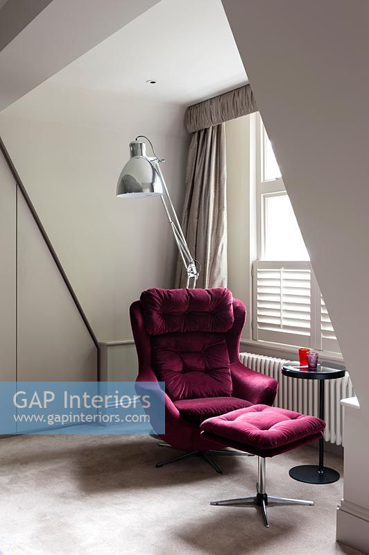 Red velvet armchair and foot stool next to window with large silver floor lamp 